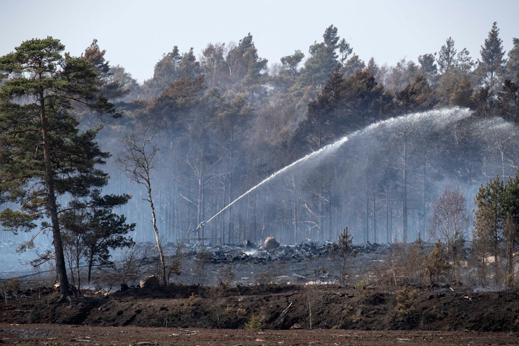 En spridare sprutar vatten över den brinnande stubbahögen på Åbuamosse utanför Hästveda där en skogsbrand rasat sedan i tisdags.