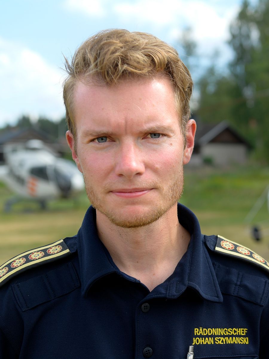 Porträtt av person i uniform utomhus med helikopter i bakgrunden.