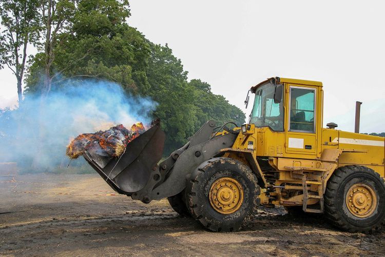 En gul traktor arbetar med att eftersläcka en brand.

