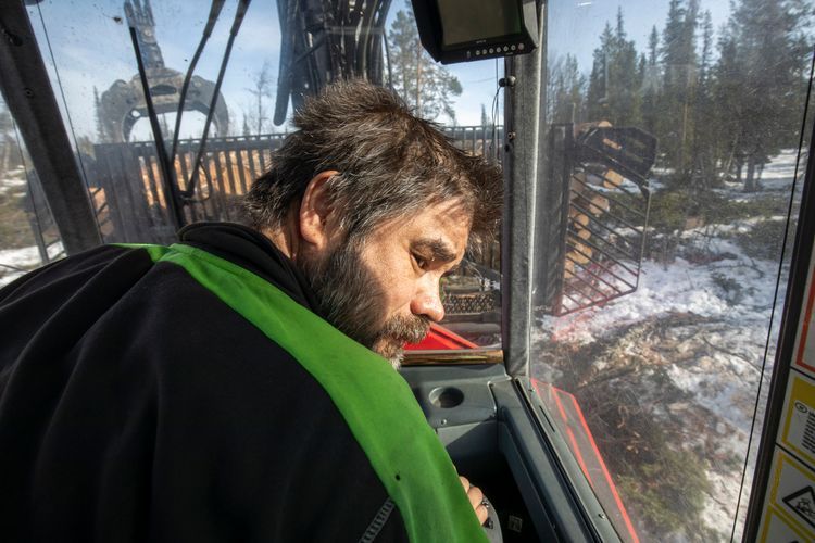 Man i skogsmaskin tittar ut genom fönstret i snötäckt skogslandskap