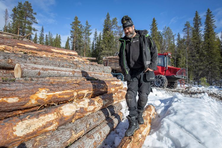 Skogsarbetare står på en hög med timmerstockar i snötäckt skogsmiljö