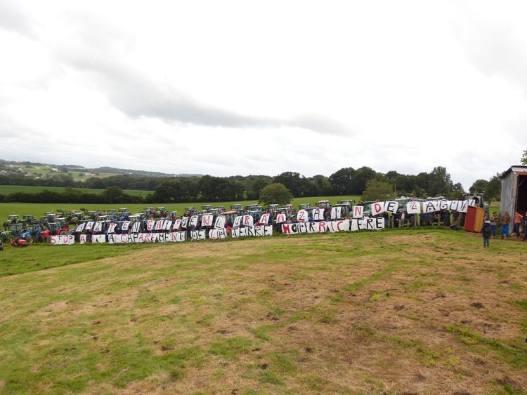 ”STOPP FÖR MARKSPEKULATIONER AV BÖRDIGA JORDAR” står det på skyltar framför uppställda traktorer på ett fält i Frankrike.