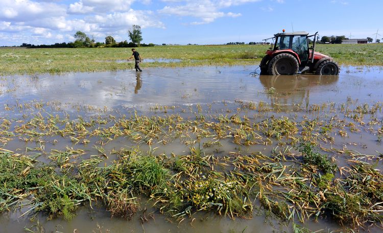 Översvämmad åker i Skåne. En röd traktor sitter fast i vattenmassan.